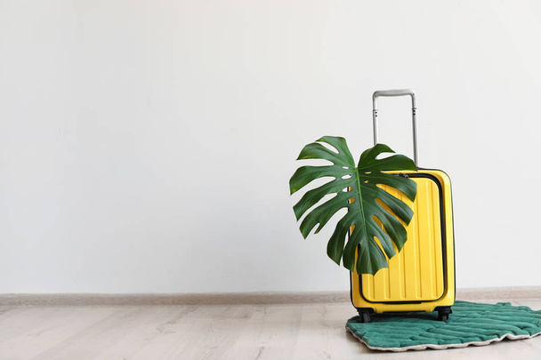 Bright yellow suitcase with tropical leaf indoors - Фото, изображение