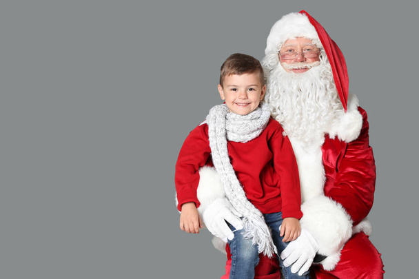 Little boy sitting on authentic Santa Claus' lap against grey background - Photo, Image