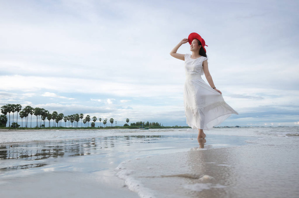 Beautiful Asian girl wearing white dress and red hat on the beach. - Photo, Image