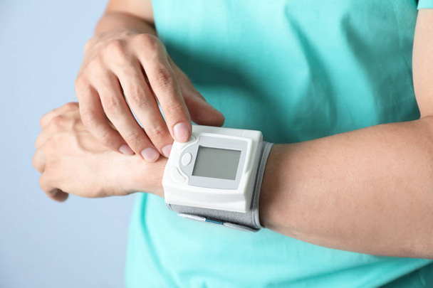 Young man checking pulse with blood pressure monitor on wrist against color background, closeup - Photo, Image