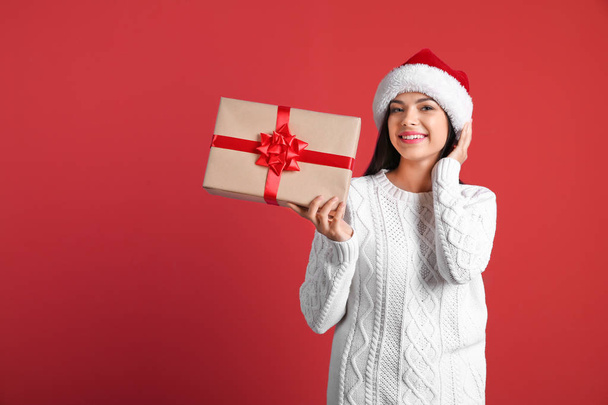Young beautiful woman in Santa hat with gift box on color background. Christmas celebration - Фото, зображення