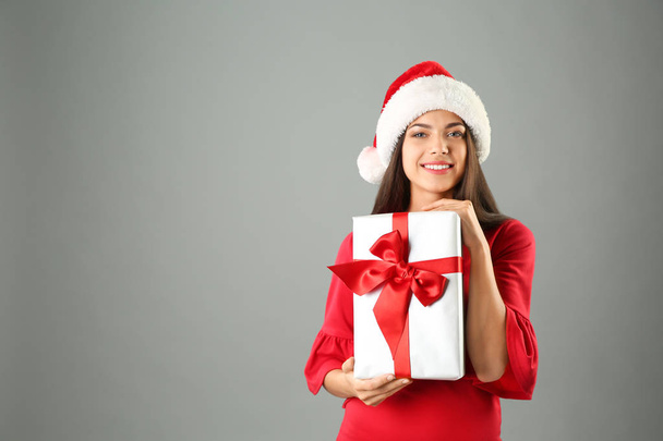 Young beautiful woman in Santa hat with gift box on grey background. Christmas celebration - Fotografie, Obrázek