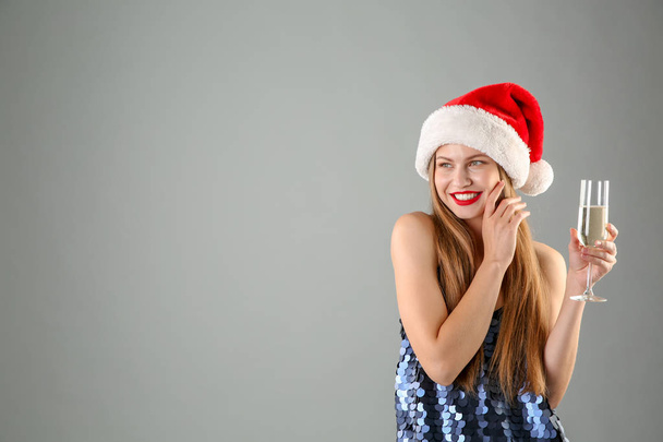 Young beautiful woman in Santa hat with glass of champagne on grey background. Christmas celebration - Foto, immagini