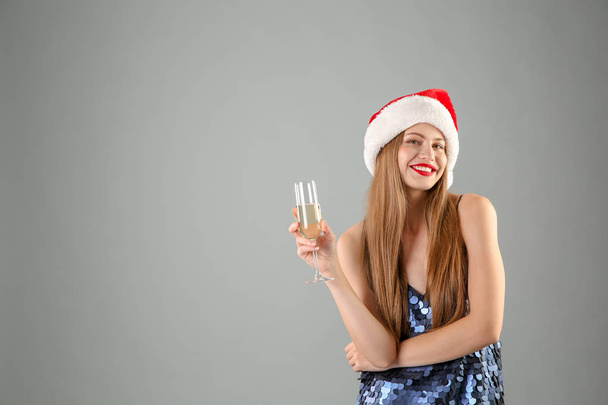 Young beautiful woman in Santa hat with glass of champagne on grey background. Christmas celebration - Foto, Bild
