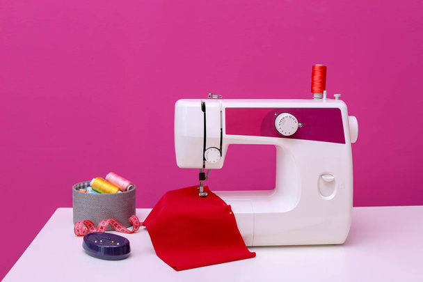 Modern sewing machine on table against color background - Foto, Imagen