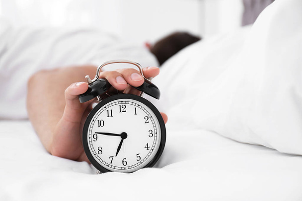 Man turning off alarm clock in bedroom - Foto, Imagen
