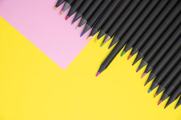 Het bovenste uitzicht op zwarte kleur potloden gekleurd in tinten van roze en geel op de achtergrond van het papier van de kleur met kopie ruimte. - Foto, afbeelding