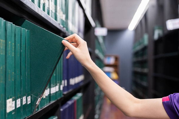 Kézzel húzza egy dolgozat könyv a könyvtárban a polcról. Zöld színek könyvek. - Fotó, kép