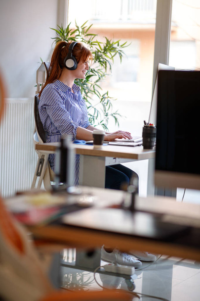 Woman with head phones working in modern office at computer - Photo, Image