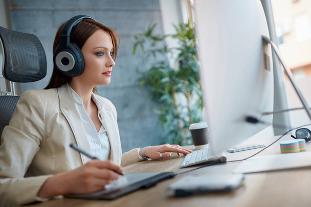 Young woman wearing headphones and working in design studio - Фото, зображення