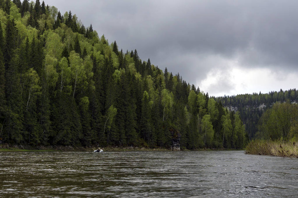 Krajina Kojva řeka Ural, Čusovaja přítok, malebné zalesněné pobřežní útesy a rybářský nafukovací člun v dálce, na zamračený den, - Fotografie, Obrázek