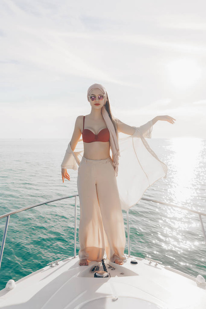 bela menina alta em óculos de sol posando em um iate branco, desfrutando de uma aventura no mar
 - Foto, Imagem