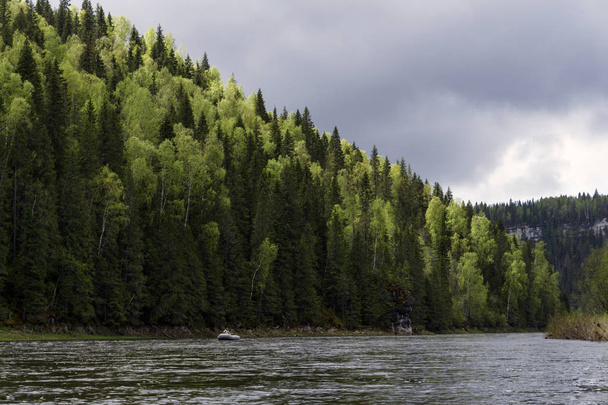 maisema Ural joen Usva, Chusovaya sivujoki, jossa viehättävä metsäinen rannikko kallioita ja kalastus puhallettava vene etäisyydellä, pilvinen päivä
, - Valokuva, kuva