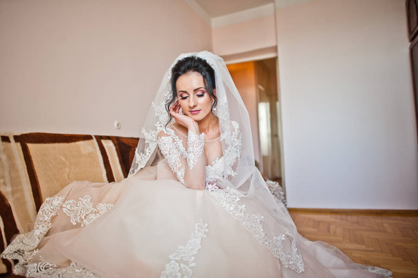 Portrait of a bride in beautiful white wedding dress sitting on the sofa indoors. - Fotografie, Obrázek