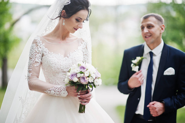 Gorgeous and happy newly married couple standing in green park on their wedding day. - 写真・画像