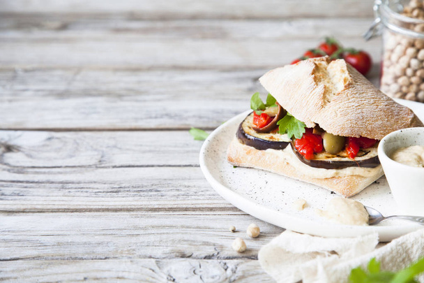 Healthy vegan sandwich with hummus, baked paprika, olives and grilled aubergine on rustic wooden background.  - Фото, изображение