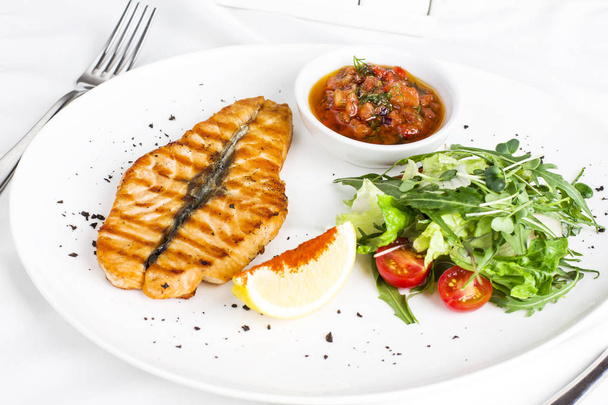 O grande bife de salmão peixe vermelho na grelha com limão, molho com legumes e verduras no prato branco
 - Foto, Imagem