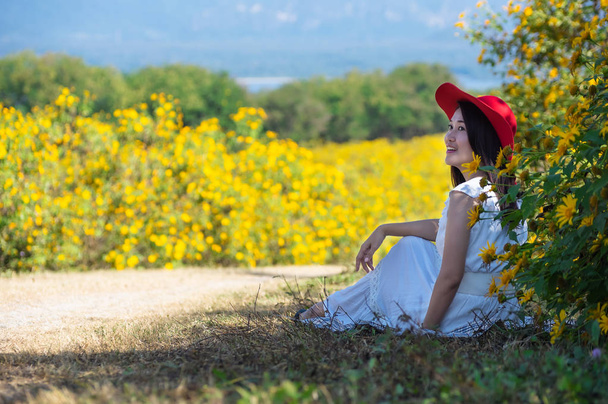 自然の花、彼女の白いドレスと赤い帽子の炭鉱、ランパーン県、タイで桐ブアトン メキシコひまわり畑の上に座ってで美しい女性. - 写真・画像