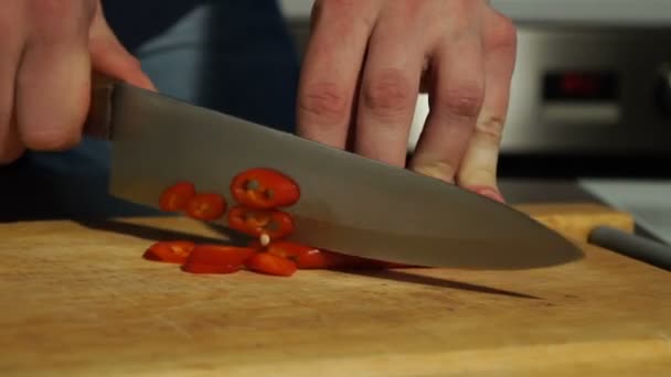 Slicing Red chili pepper. A man cuts pepper on a wooden Board - Felvétel, videó