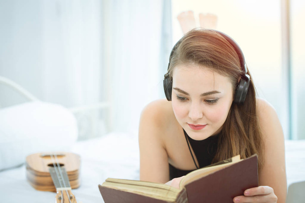 Ragazza sdraiata sul letto a leggere libro e ascoltare musica sulle cuffie per rilassarsi
. - Foto, immagini