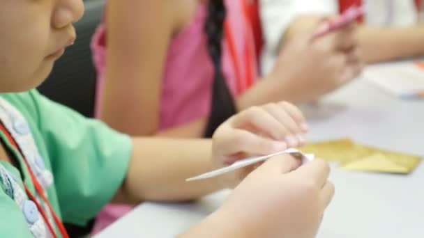 4К: Азиатский ребенок учится складывать японские бумажные оригами, искусство складывания бумаги, которое часто ассоциируется с японской культурой
. - Кадры, видео