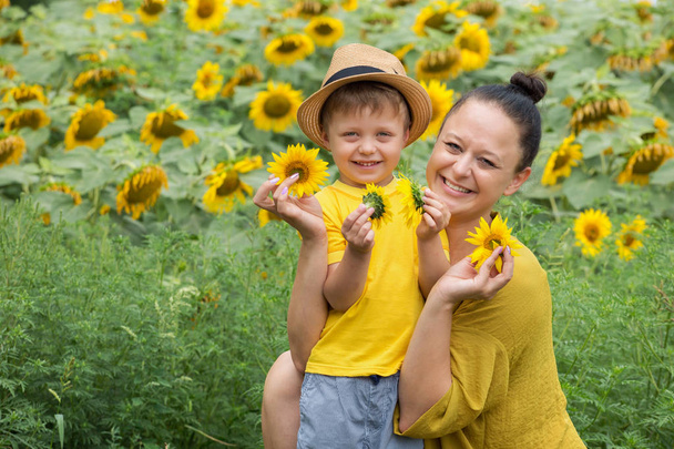 Mom and son hug, laugh and play in a field of sunflowers. Happy family moments spent in the open air. Mother's Day. - Foto, Imagem