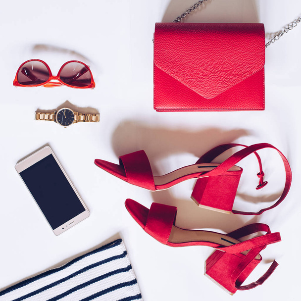 Modeblog-Konzept auf weißem Hintergrund. flache Verlegung eines minimalen Sets weiblicher Accessoires: goldene Armbanduhr, rote Sandalen mit Knöchelriemen, Handtasche, Handy, Sonnenbrille, gestreiftes Hemd - Foto, Bild