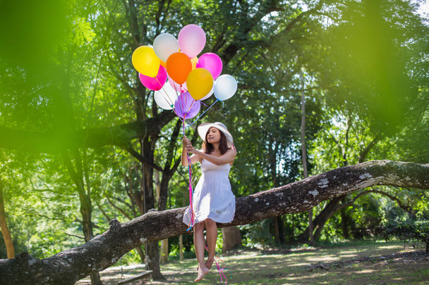 Joven adolescente sentada en el árbol y sosteniendo globos en la mano
 - Foto, Imagen