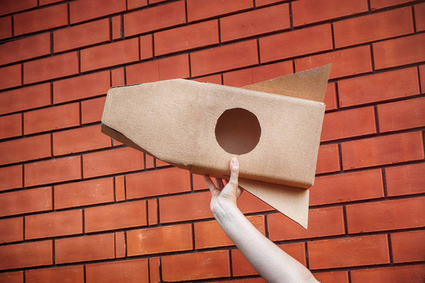 Cardboard space rocket in hand against brick wall - Fotografie, Obrázek