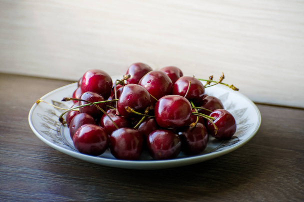 Fresh tasty cherry fruit on a plate on a wooden table - Zdjęcie, obraz