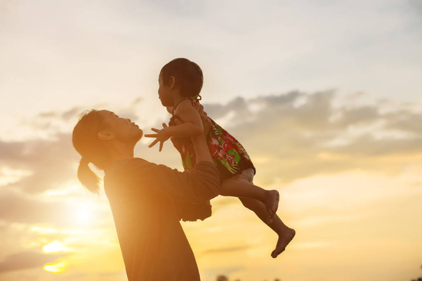 una silueta de un niño joven y feliz los brazos de su madre cariñosa para un abrazo, frente a la puesta de sol en el cielo en un día de verano
. - Foto, imagen