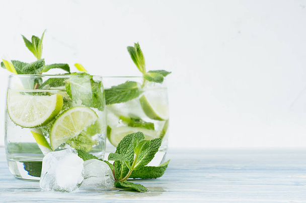 Tropical fresh cold cocktail gin tonic with mint, lime, ice, straw on light blue shabby wood board and white background, copy space. - Foto, Imagen