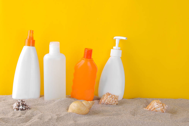 Verschillende flessen met zonnebrandmiddelen en schelpen in het zand op een gele achtergrond - Foto, afbeelding