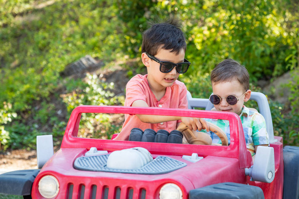 Молодые смешанные расы китайские и кавказские братья в солнечных очках, играющие в игрушечном автомобиле
 - Фото, изображение