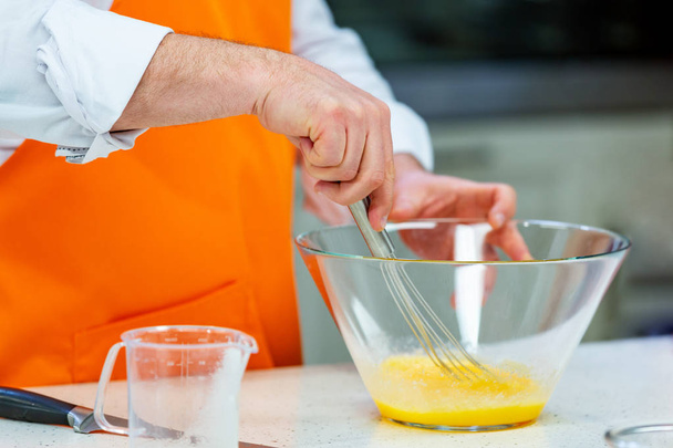 Küchenzubereitung: Der Koch schlägt Eier in einer Schüssel mit dem Schneebesen. - Foto, Bild