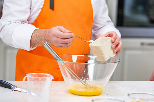 Küchenzubereitung: Der Koch fügt den geschlagenen Eiern Zucker hinzu - Foto, Bild