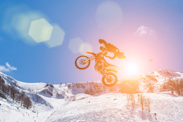 corredor en una motocicleta en vuelo, salta y despega en un trampolín contra las montañas nevadas
 - Foto, imagen