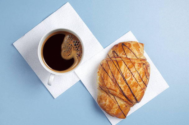 Cup of coffee and croissant with chocolate on blue table, top view - Foto, immagini