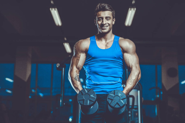 Handsome young fit muscular caucasian man of model appearance workout training in the gym gaining weight pumping up muscles and poses fitness and bodybuilding sport concept - Foto, Imagem