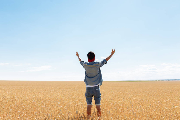 the man raised his hands to the sky, against the background of a wheat field, the guy in the cap and shirt - Fotó, kép