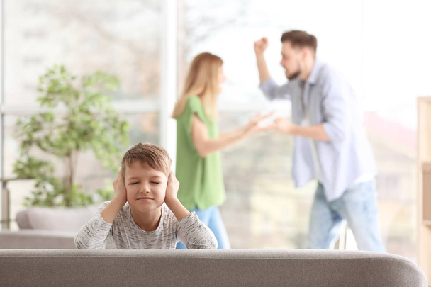Little unhappy boy sitting on sofa while parents arguing at home - Fotó, kép