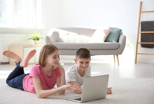 Teenage girl and her brother with laptop lying on cozy carpet at home - Foto, Bild