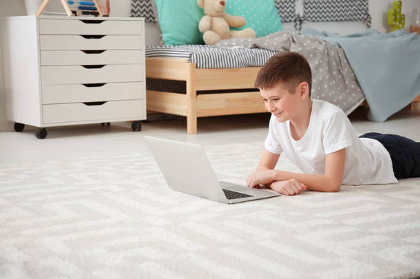 Happy boy with laptop lying on cozy carpet at home - Фото, зображення