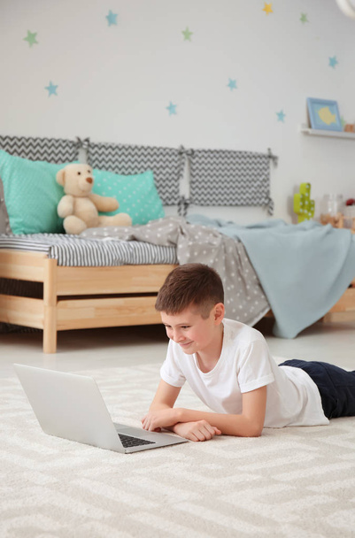 Happy boy with laptop lying on cozy carpet at home - Photo, Image
