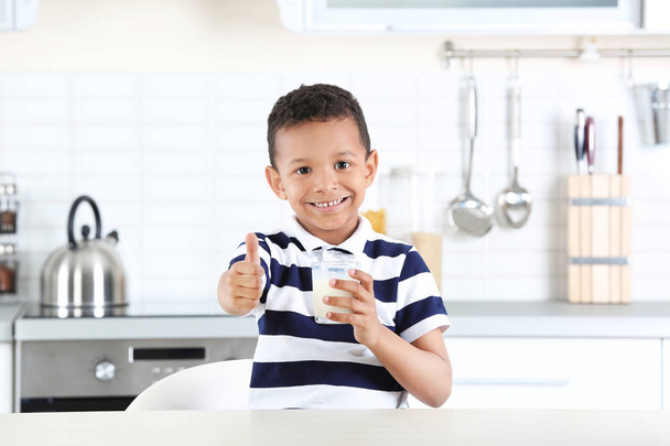 Adorable African-American boy with glass of milk in kitchen - 写真・画像