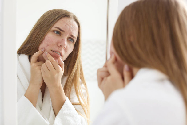 Young woman with acne problem near mirror in bathroom - Zdjęcie, obraz