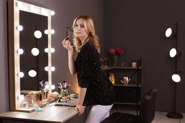 Young woman applying makeup near mirror in dressing room - Фото, зображення