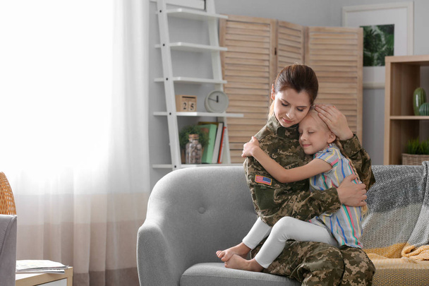 Woman in military uniform with her little daughter on sofa at home - Foto, Bild