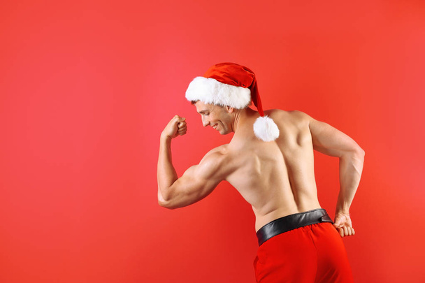 Young muscular man in Santa hat on color background - Φωτογραφία, εικόνα