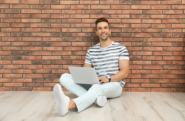 Man in casual clothes with laptop near brick wall - Фото, зображення